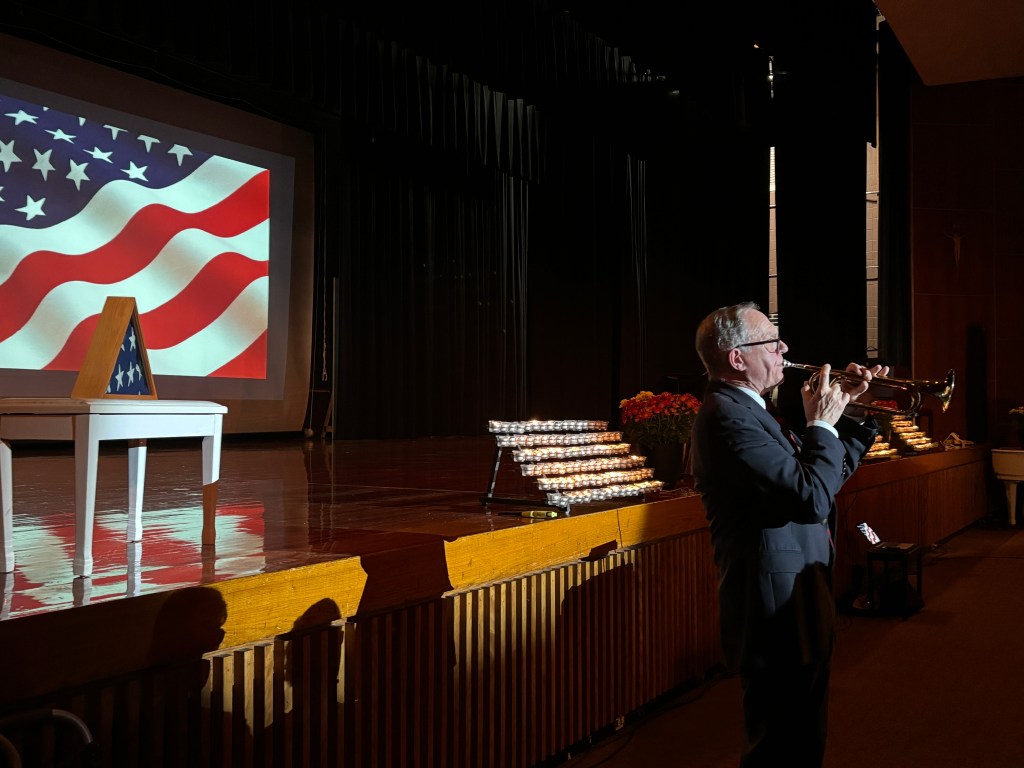 a trumpet player performing in front of a stage displaying the american flag